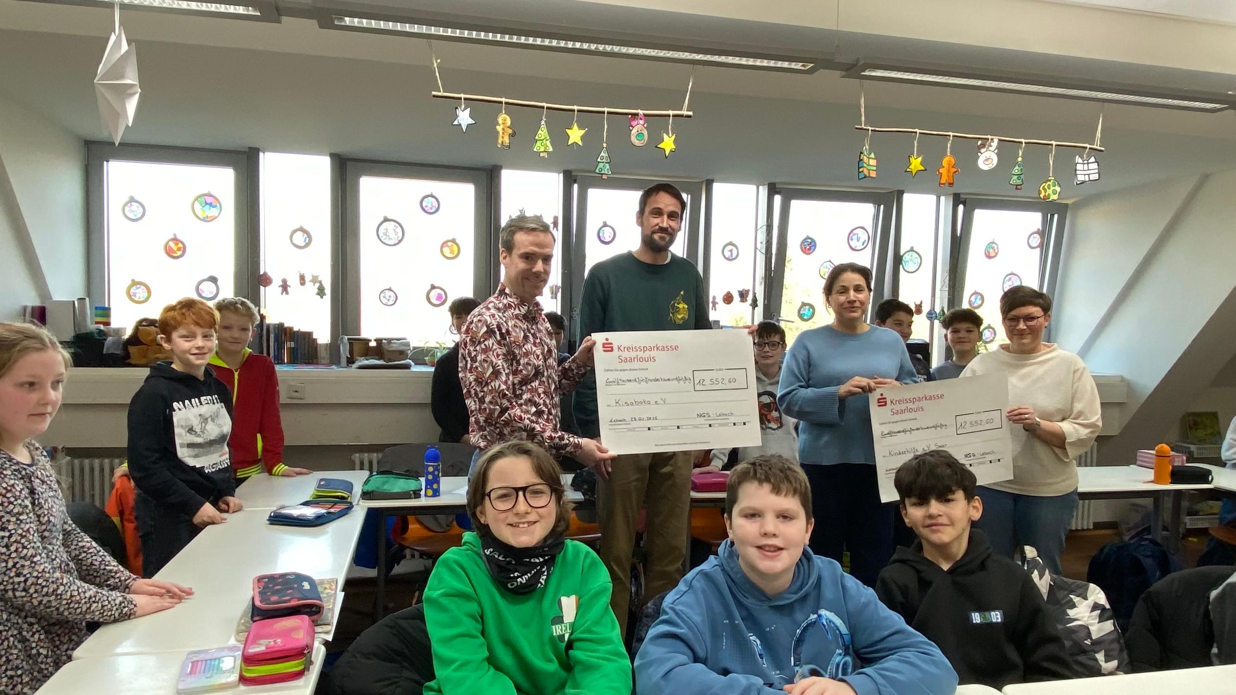 Schülerinnen und Schüler sowie Lehrkräfte der Nikolaus Groß-Schulen in Lebach überreichen Antonia Nutting von Boch (Kinderhilfe Saar) und Lukas Schäfer (Verein Kisoboka, Uganda) symbolisch Schecks mit den Erlösen ihres Spendenlaufs.