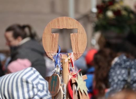 Heilig-Rock-PIlgerstab aus Holz mit bunten Fahnen, im Hintergrund Pilgergruppe