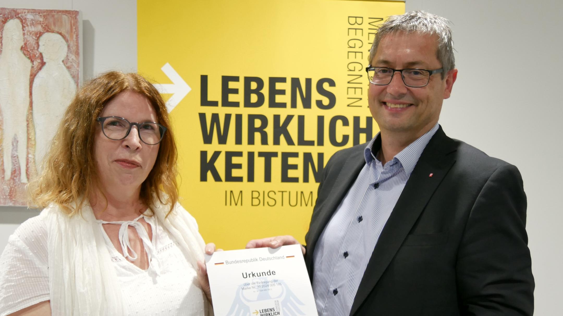 Dr. Martina Messan (Programmleiterin) und Diözesan-Caritasdirektor Christoph Wutz präsentieren stolz die Urkunde zur Markeneintragung.