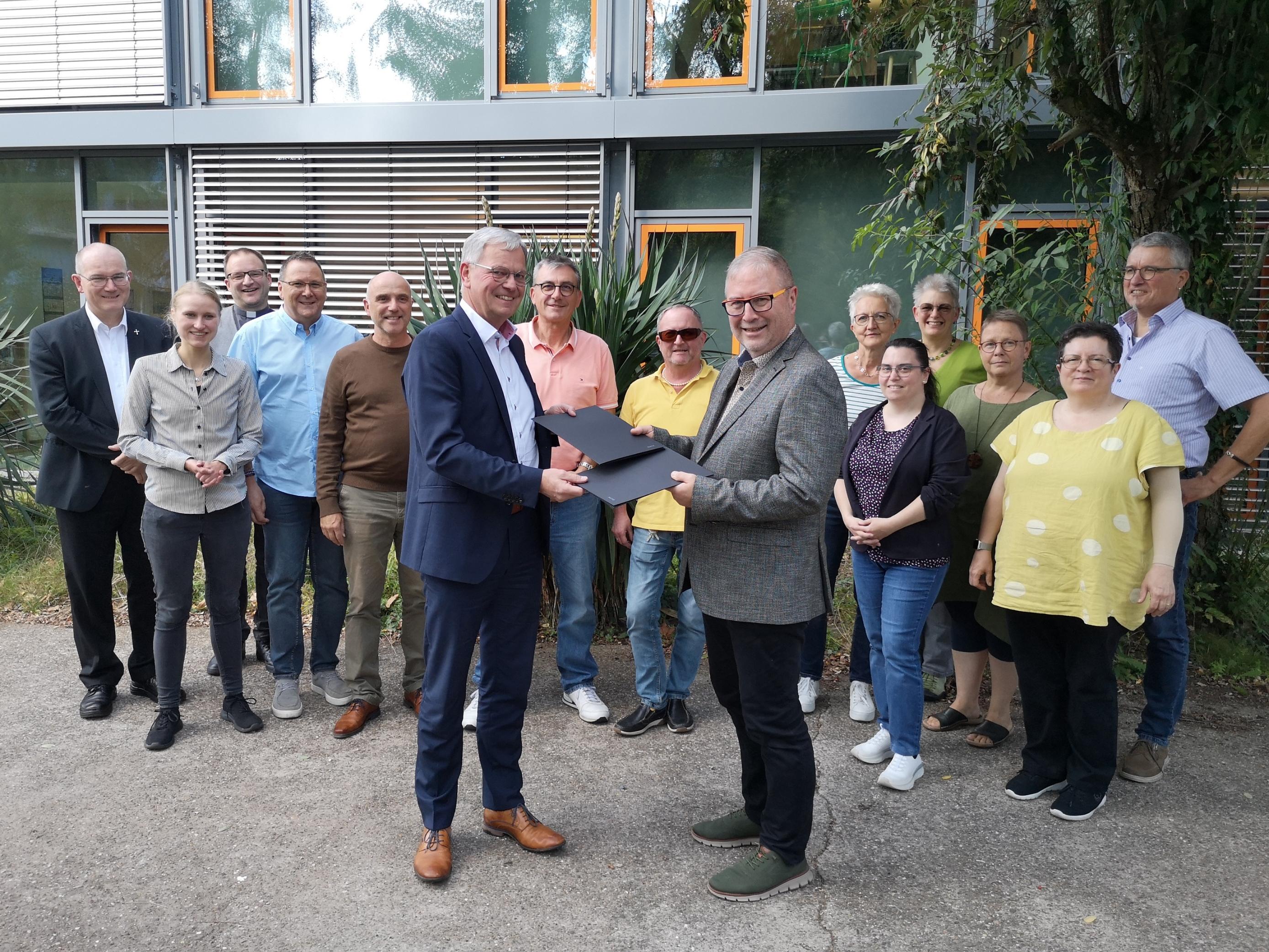 Generalvikar Dr. Ulrich Graf von Plettenberg (v.l.) und Superintendent Christian Weyer (v.r.) nehmen wechselseitig die unterzeichnete Kooperationsvereinbarung zur Krankenhausseelsorge in Empfang. Dahinter Vertretende der Klinikseelsorgenden im Saarland