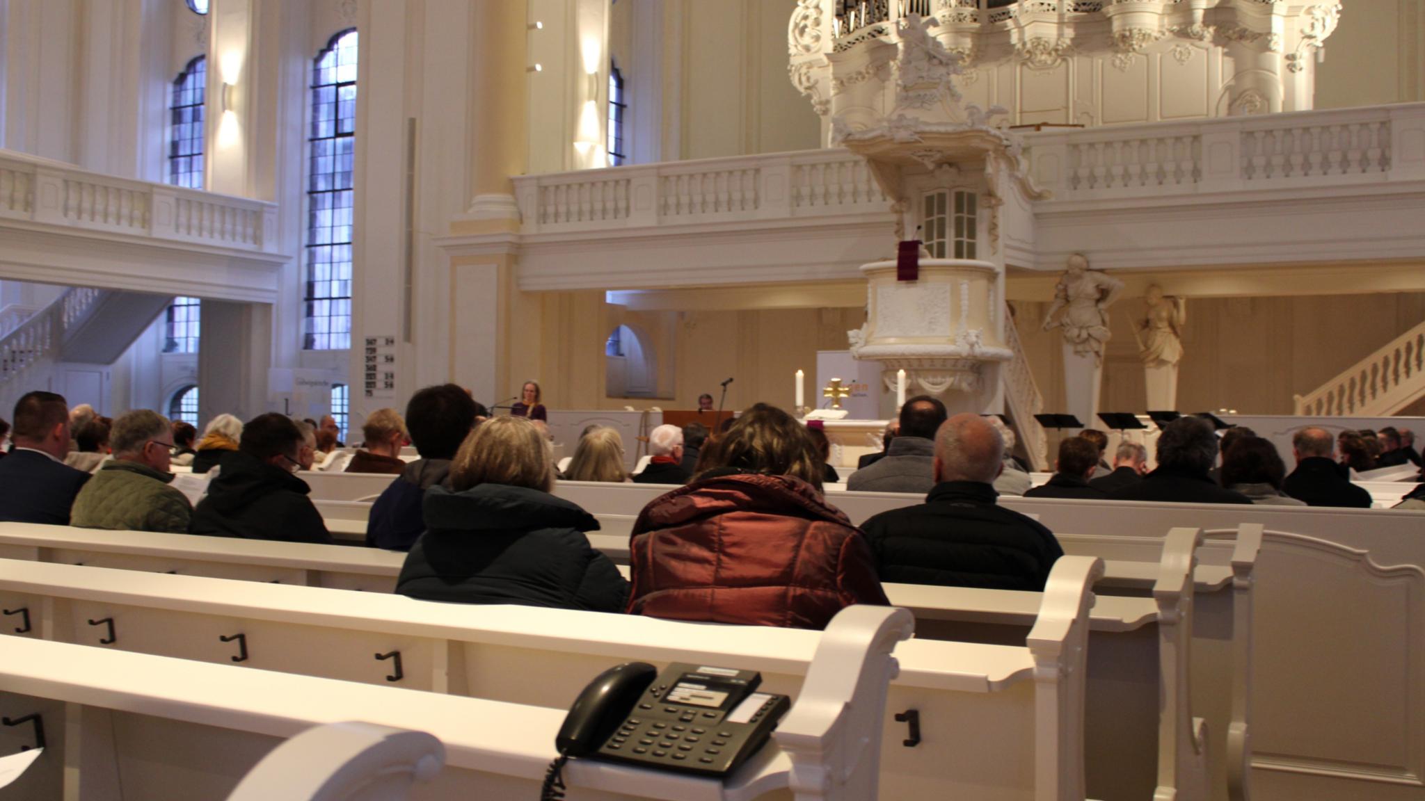 Menschen sitzen in den Kirchenbänken, auf den Bänken stehen Telefone