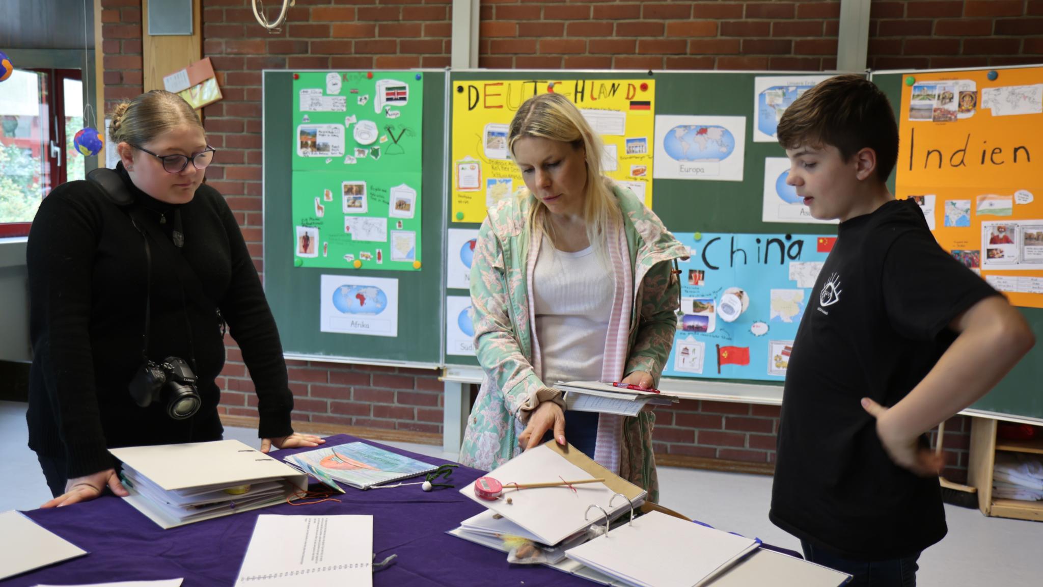Die Schülerin Mary (rechts) und Schüler Kim (links) zeigen Kathrin Schmitt von der Trierischen Tonpost ihre Buch-Übersetzungen.