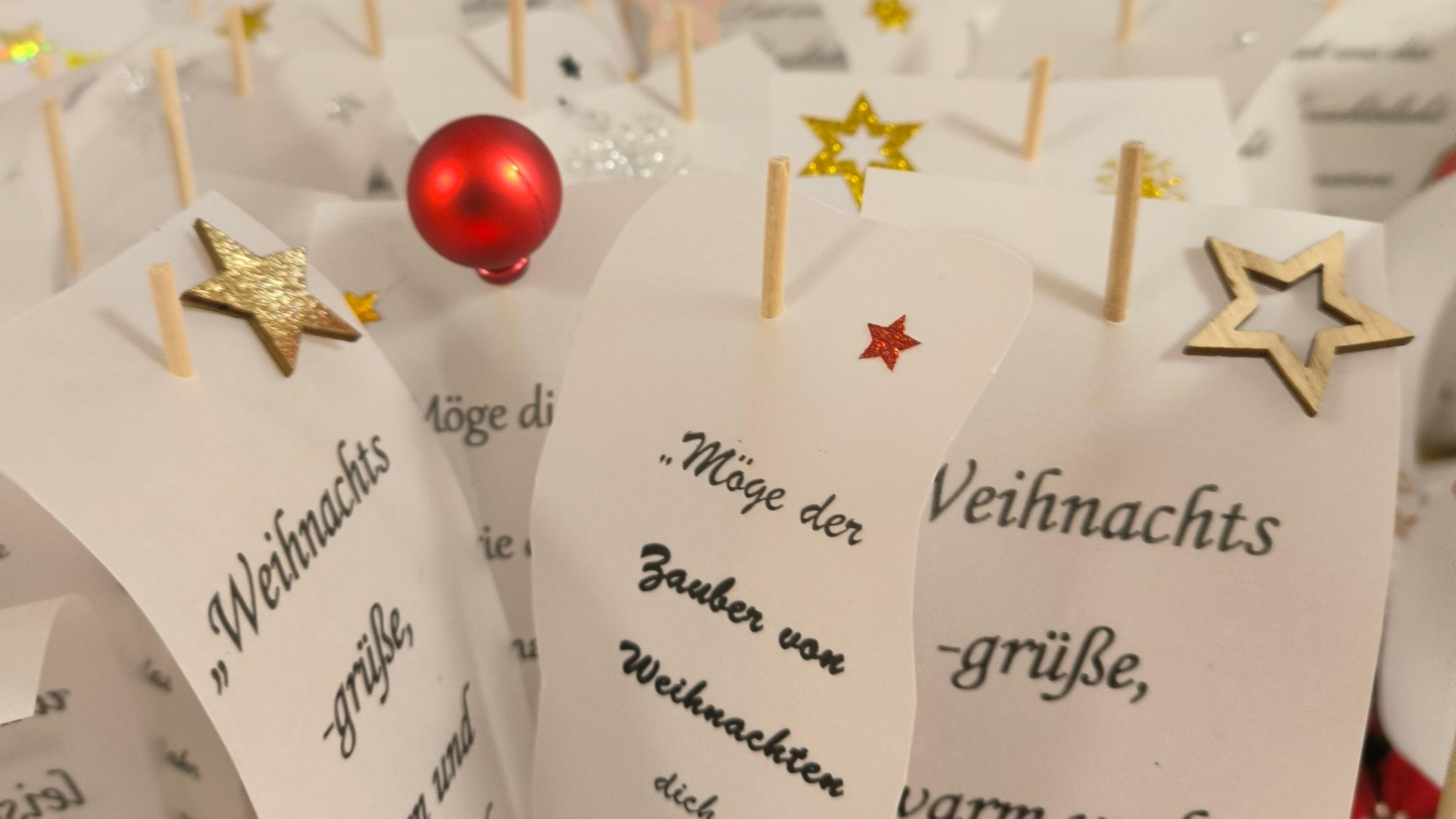 Mehrere kleine Kärtchen mit Weihnachtsgrüßen, verziert mit bunten Sternen und Kugeln, stehen dicht aneinander wie ein festlicher Grußgarten