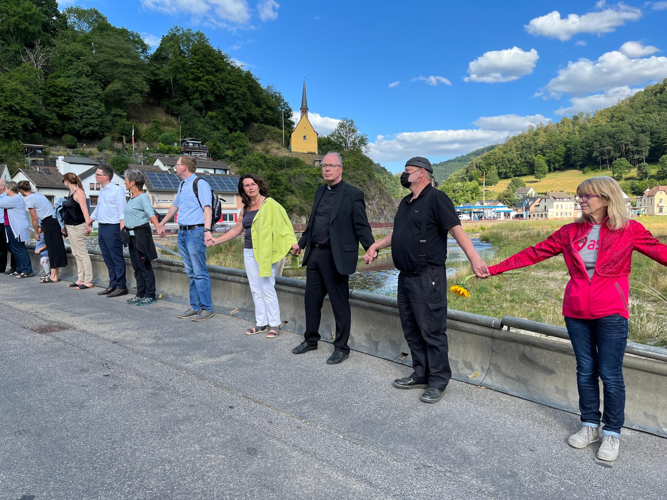 Menschenkette mit Bischof Ackermann und vielen Männern und Frauen auf der Brücke von Ahrbrück zum ersten Jahresgedenken der Flutkatastrophe.