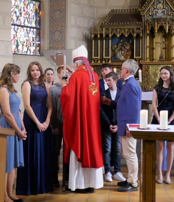 Mehrere junge Menschen stehen in einer Kirche und werden vom Weihbischof gesegnet.