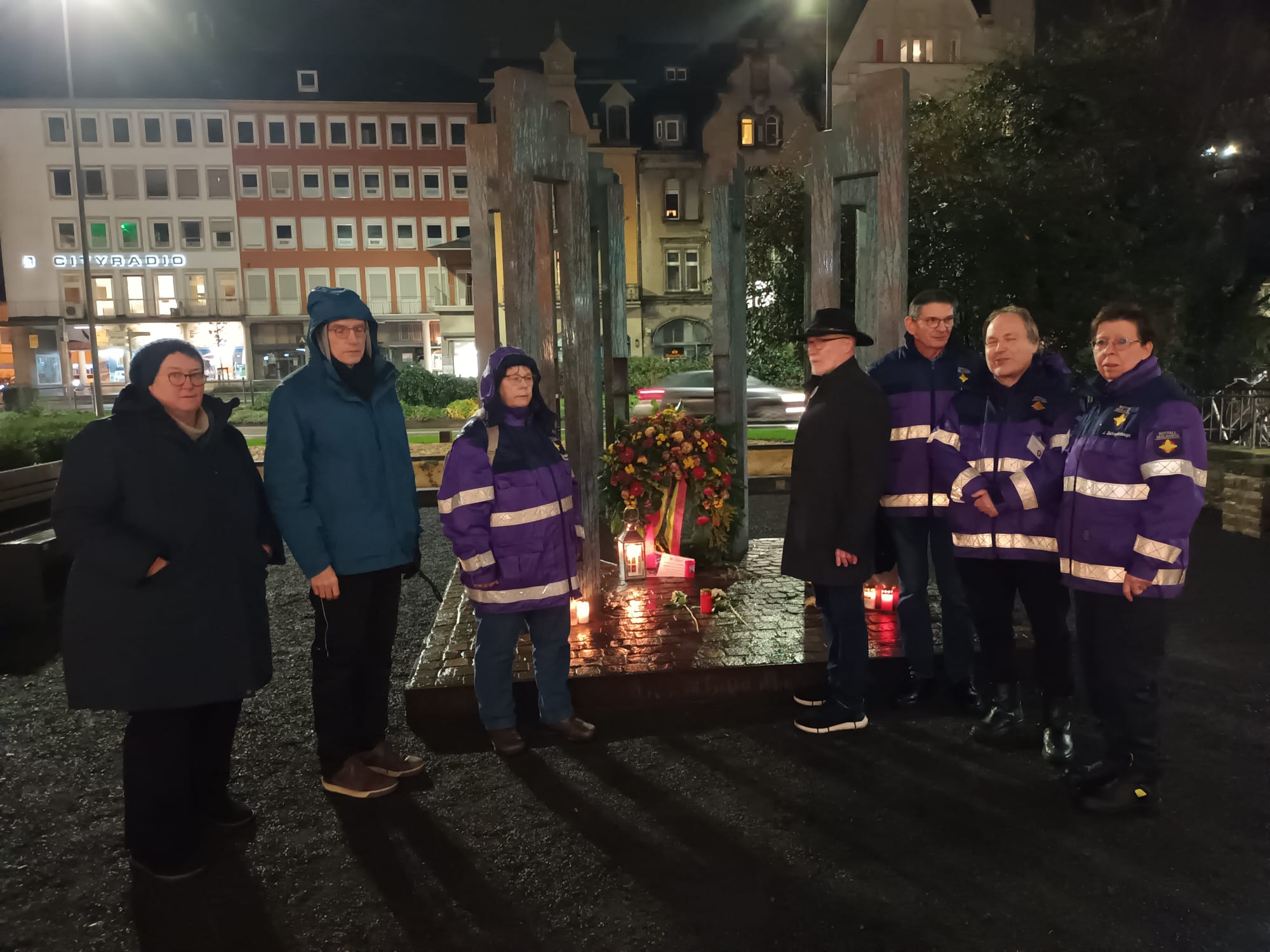 Zu sehen sind Notfallseelsorger*innen und weitere Teilnehmende des Gedenkens an die Opfer des Anschlags in Magdeburg an der Gedenkstätte der Amokfahrt von 2020 in Trier (21.12.2024).