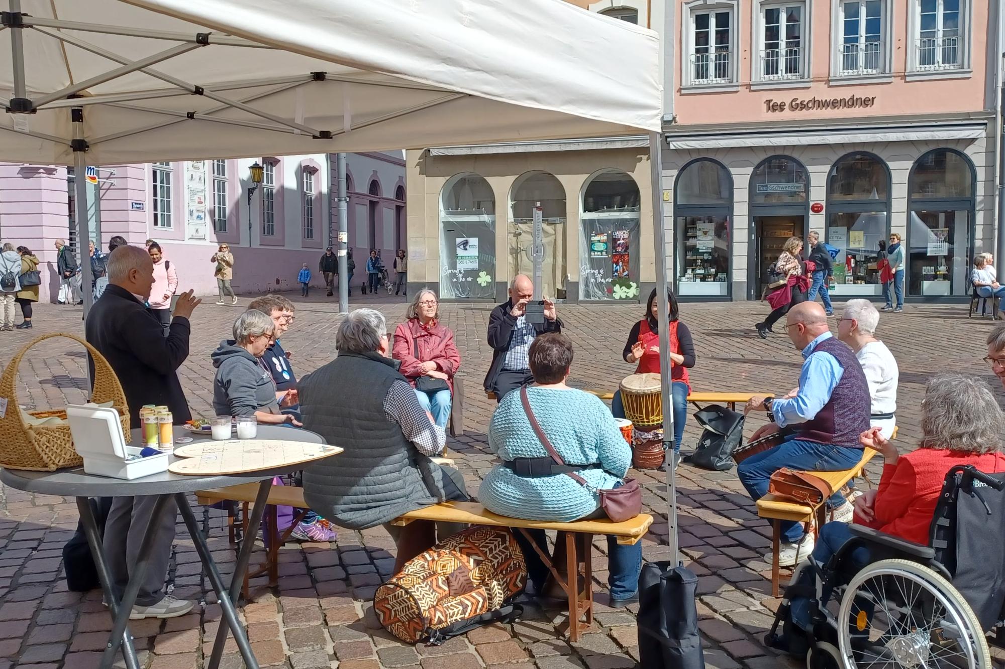 Das Bild zeigt Teilnehmer eines TrDas Bild zeigt an den Heilig Rock Tagen 2023 Menschen unterschiedlichen Alters und Geschlechts an dem Stand zum Thema Inklusion. Sie nehmen an einem inklusiven Trommelworkshop teil.