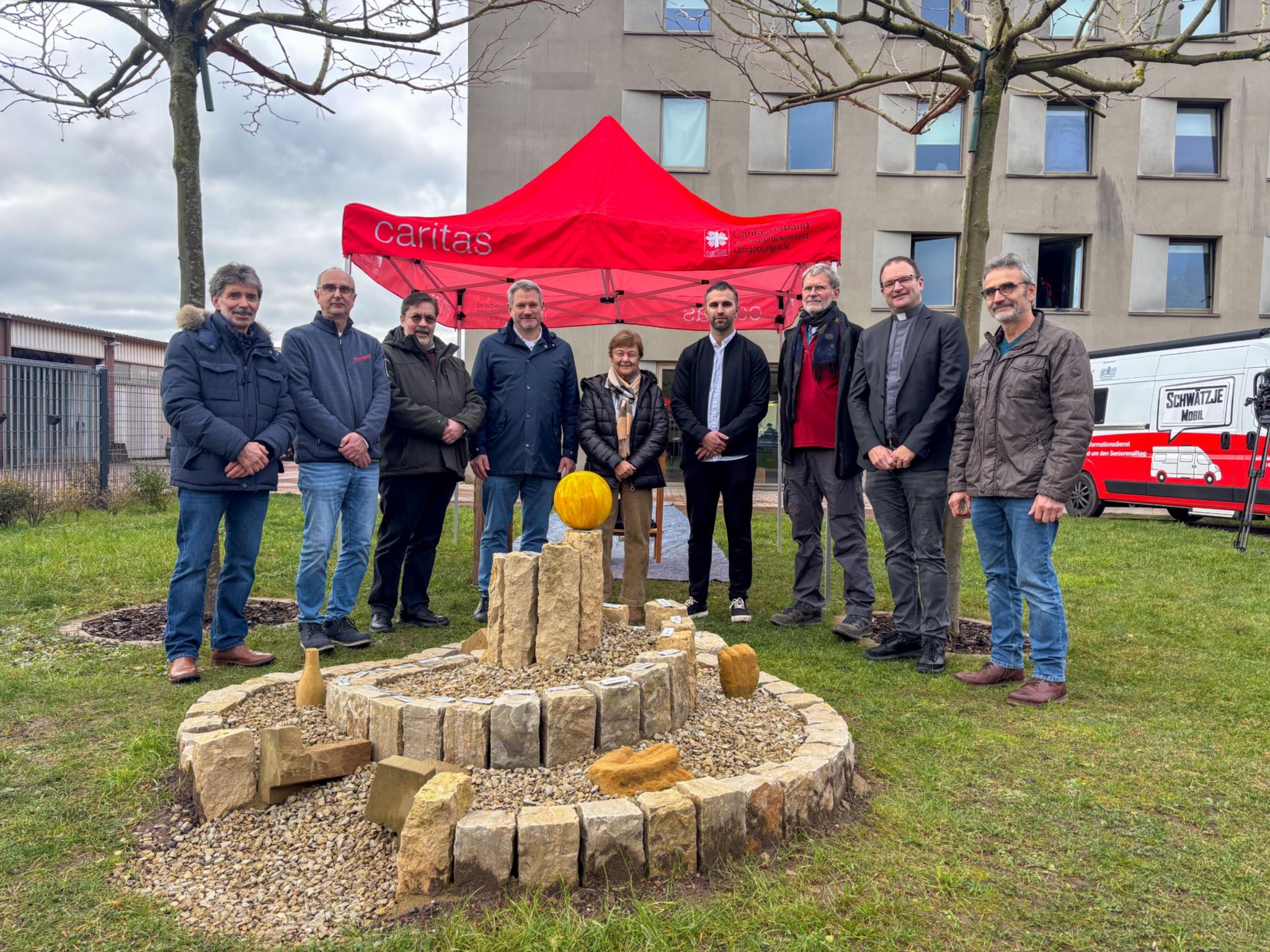Acht Personen stehen vor einem Zelt der Caritas für ein Gruppenbild zusammen